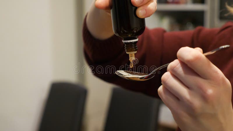 Female pouring and counting herbal medicine drops to spoon at home