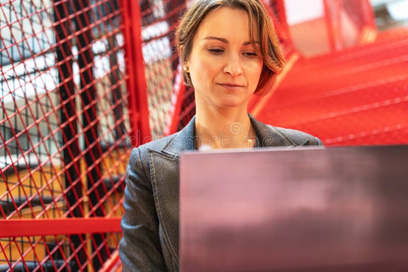Female programmer working on code in modern office with industrial red stairs royalty free stock image