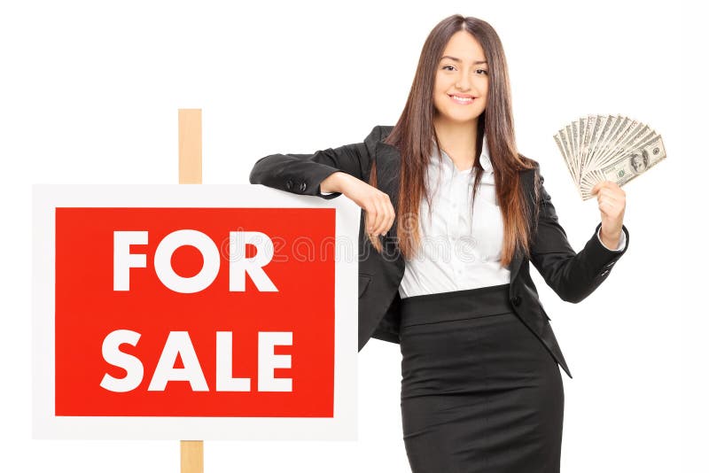Female real estate agent holding money by a for sale sign isolated against white background