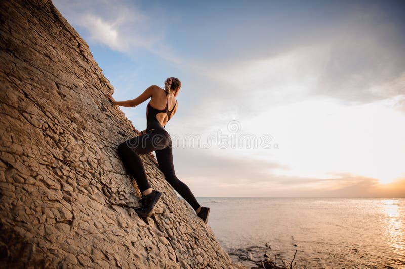 Female rock climber watching sunset over sea