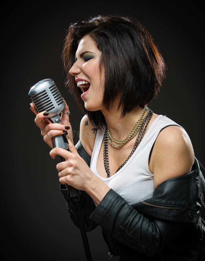 Half-length portrait of female rock singer wearing black jacket and holding microphone on grey background. Concept of music and rave. Half-length portrait of female rock singer wearing black jacket and holding microphone on grey background. Concept of music and rave