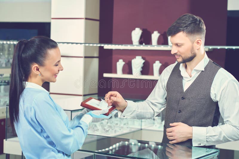 Female seller in jewelry store showing golden ring for buyer.