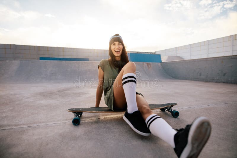 Smiling woman skateboarder sitting on her long board. Female skater having fun at skate park.