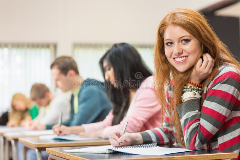 Female student with others writing notes in classroom stock image