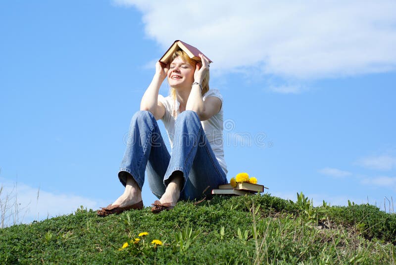 Female student outdoor on green grass with books