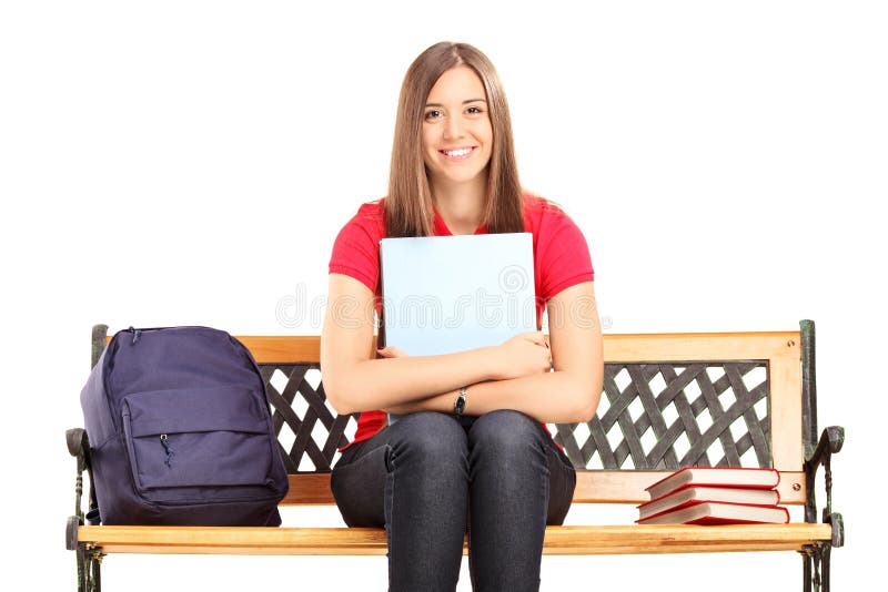 Female student sitting on a wooden bench and holding a notebook isolated on white background