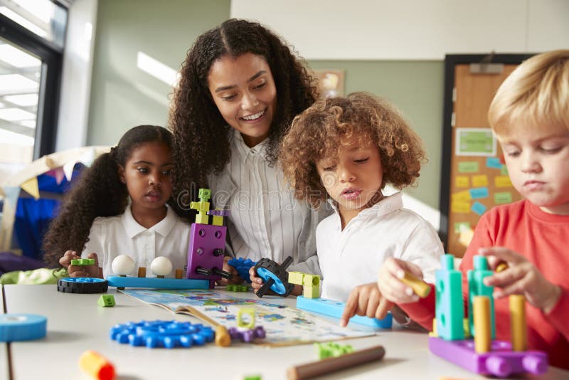 Female teacher sitting at table in play room with three kindergartne children constructing, selective focus