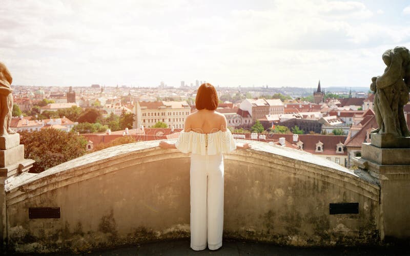 Young female tourist enjoying great view on the old town of Prague, city streets during sunset. Golden hour time for photo