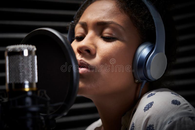 Female Vocalist Wearing Headphones Singing Into Microphone In Recording Studio