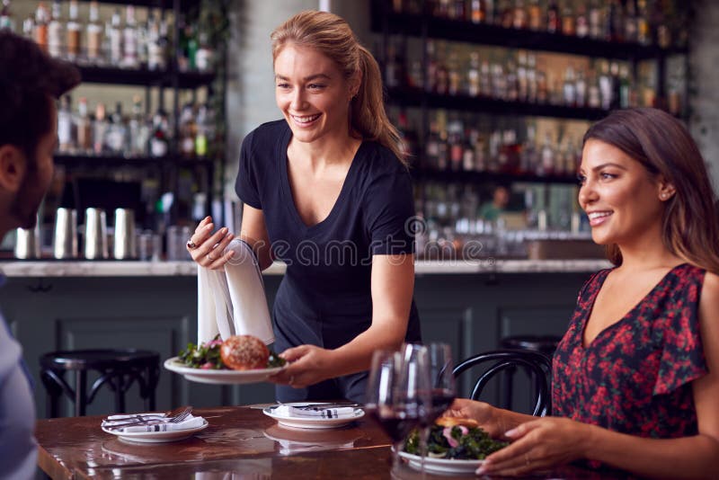 Female Waitress Serving Food To Romantic Couple Sitting At Restaurant