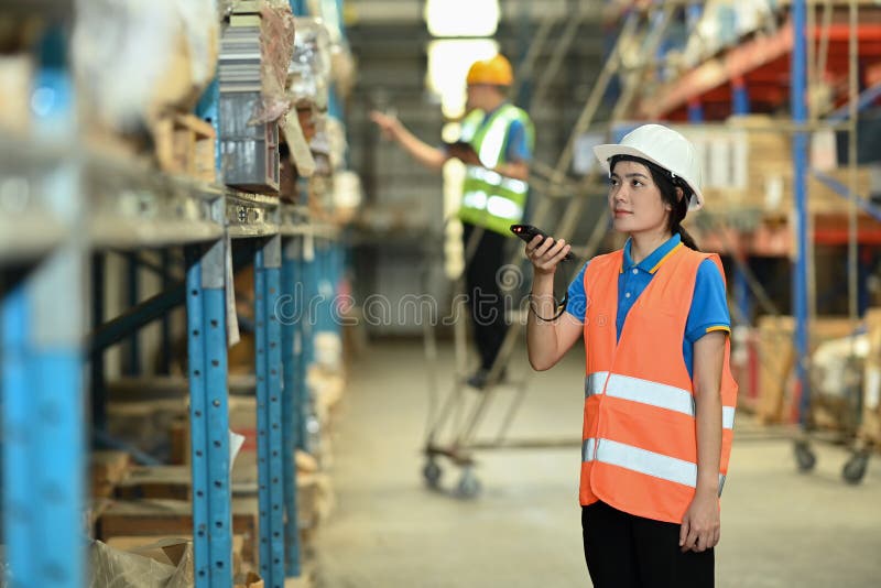 Female workers wearing hardhats and vests checking inventory boxes on shelf with barcode scanner stock photography