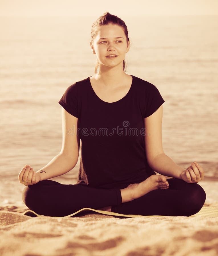 Female 20-30 years old is sitting and doing meditation in black. 