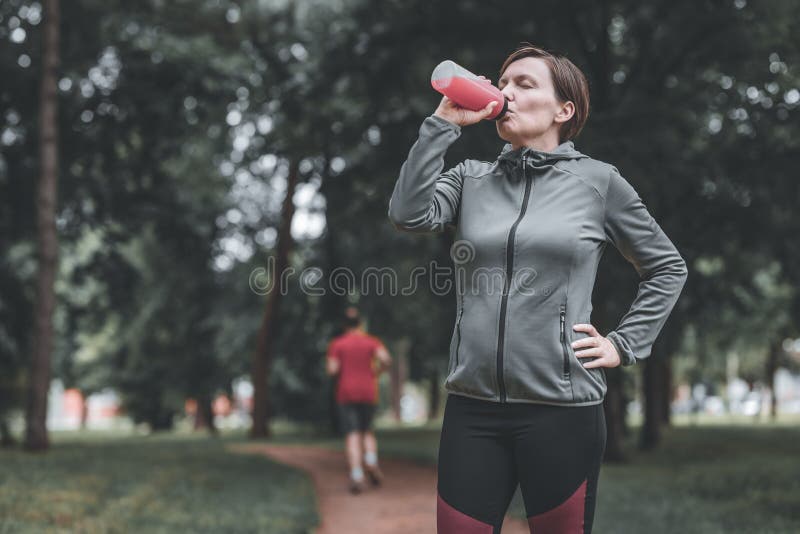 Femeie alergător băut suc de căpșuni reîmprospătat în parc stock image
