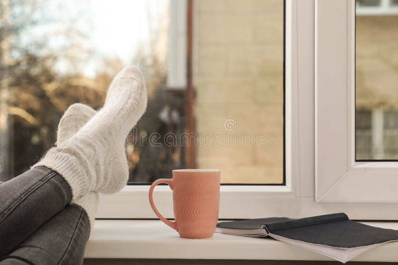 Femeie cu o ceașcă de băutură de iarnă și carnețel în apropierea ferestrei stock images