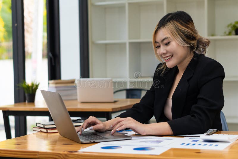 Femeie de afaceri din Asia tânără care lucrează la un computer de tip notebook cu un calculator într-un birou modern strălucitor. royalty free stock photo