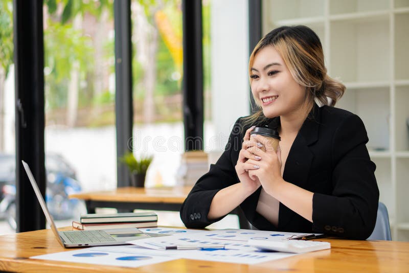 Femeie de afaceri din Asia tânără care lucrează la un computer de tip notebook cu un calculator într-un birou modern strălucitor. stock photography