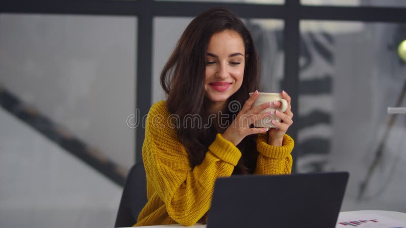 Femeie de afaceri închisă care caută un laptop. fată zâmbitoare care bea ceai lângă notebook stock video footage