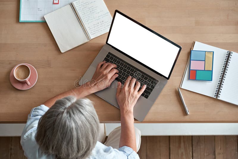 Femeie matură de vârstă mijlocie, care utilizează un computer de tip notebook care stă la locul de muncă în vedere de sus. royalty free stock image