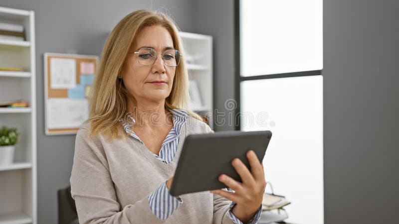 Femeie matură în birou care citește comprimate în spații închise, persoană cu experiență profesională în domeniul caucazului royalty free stock photography