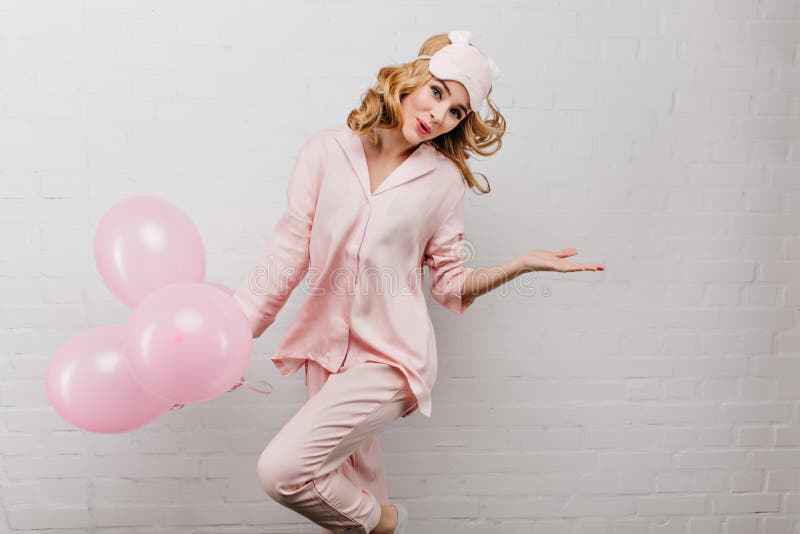 Femeie rafinată în pijamale roz dansând cu plăcere pe fond alb. fată de aniversare elegantă sărind cu royalty free stock image