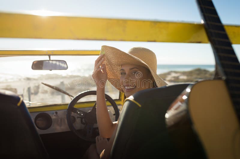 Femeie stând în galben dune buggy la plaja de nisip reglând pălărie de paie și ajungând spre chitară stock photography