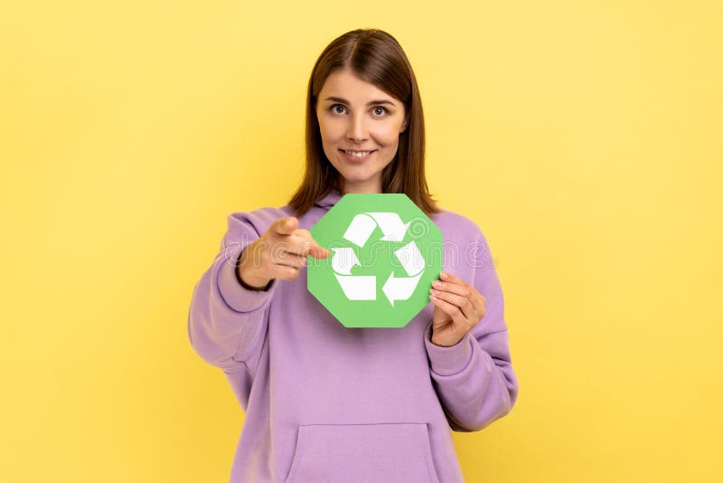 Femeie zâmbitoare care ține un panou de reciclare verde care arată cu degetul spre tine uitându-te la cameră. royalty free stock photography