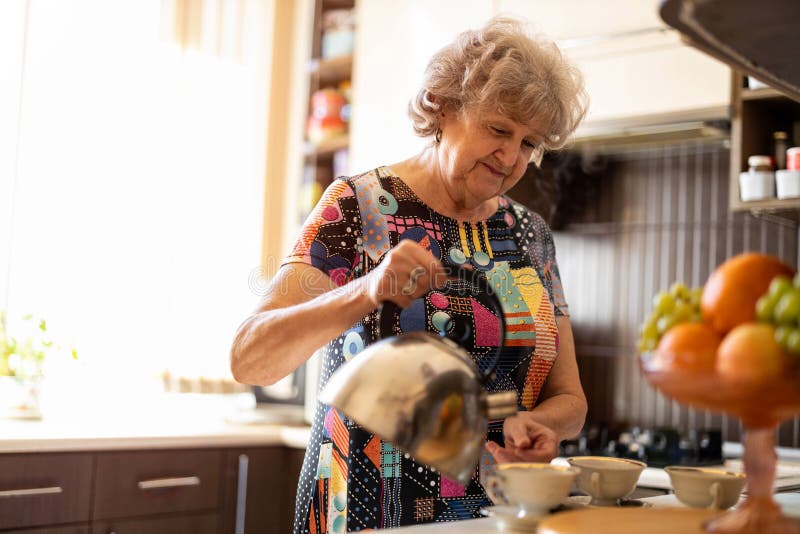 Femeie în vârstă cu ceainic turnând apă fierbinte în cupă stock photos