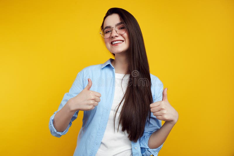 Femelle attirante gaie avec des lunettes montrant des pouces d'isolement sur le fond jaune images stock Femelle attirante gaie avec des lunettes montrant des pouces d'isolement sur le fond jaune images stock