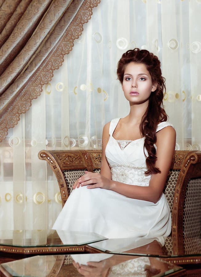 Feminidad. Novia de la mujer del pelo de Brown en la sentada del vestido de boda. Interior romántico clásico
