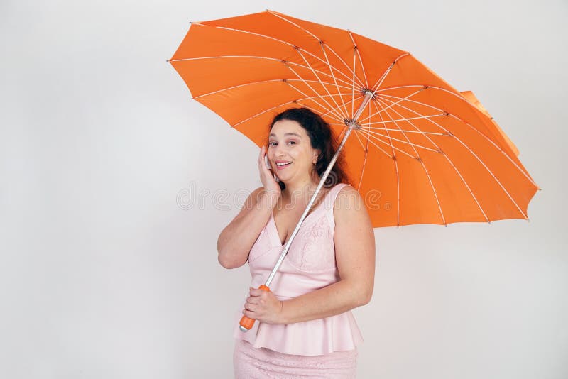 Feminine woman with plus size body in pink dress with orange big heart shaped umbrella posing on white background in Studio royalty free stock images Feminine woman with plus size body in pink dress with orange big heart shaped umbrella posing on white background in Studio royalty free stock images