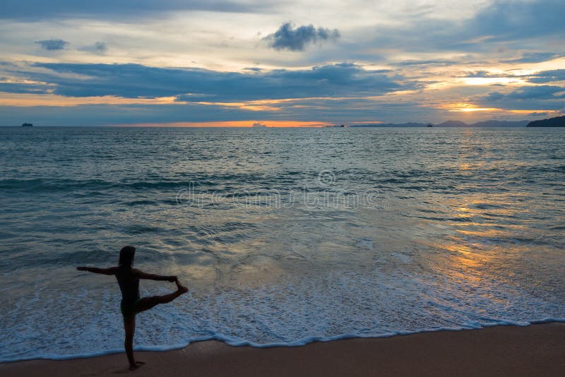 Femme active faisant le yoga sur la plage au coucher du soleil photographie stock Femme active faisant le yoga sur la plage au coucher du soleil photographie stock