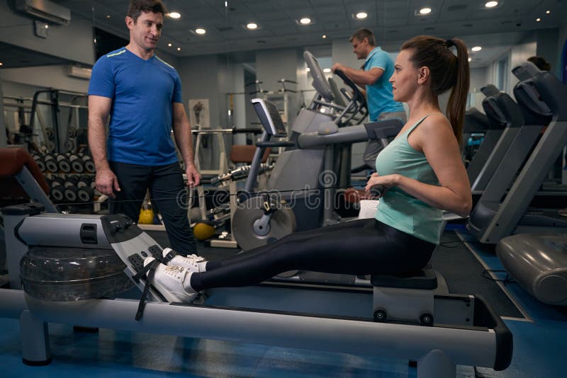 Femme adulte faisant de l'exercice sur un équipement de fitness guidé par un instructeur de gym photographie stock