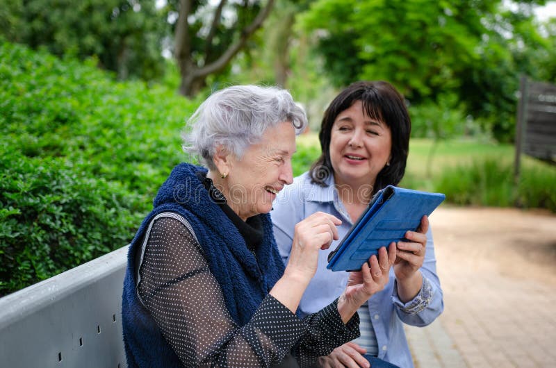 Femme adulte supérieure étant présentée pour marquer sur tablette avec l'aide volontaire photographie stock libre de droits Femme adulte supérieure étant présentée pour marquer sur tablette avec l'aide volontaire photographie stock libre de droits
