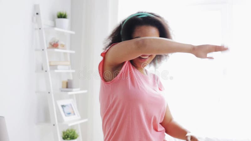 Femme africaine heureuse dans des écouteurs dansant à la maison