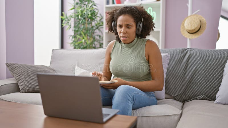 Femme afro-américaine avec casque utilisant ordinateur portable et smartphone sur canapé images libres de droits
