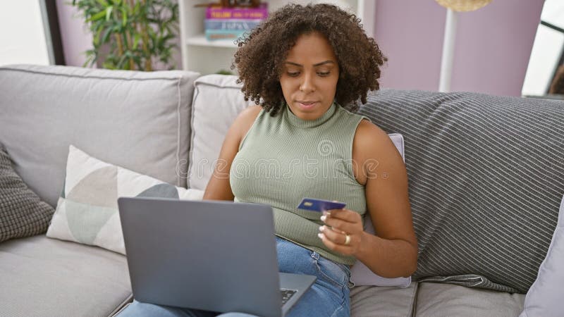 Femme afro-américaine avec ordinateur portable et carte de crédit sur canapé photo libre de droits
