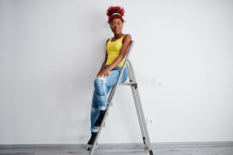 Femme afro-américaine en singlet jaune et lunettes contre mur blanc stand om échelle en fer photo libre de droits