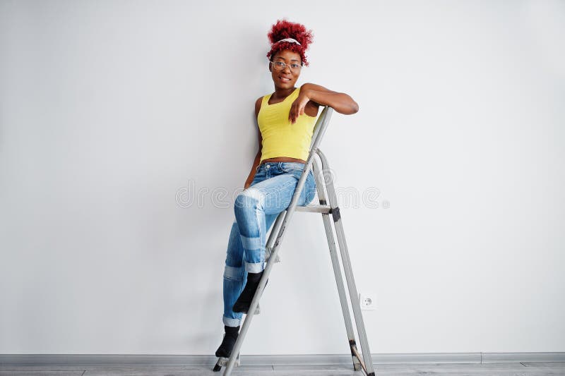 Femme afro-américaine en singlet jaune et lunettes contre mur blanc stand om échelle en fer images libres de droits