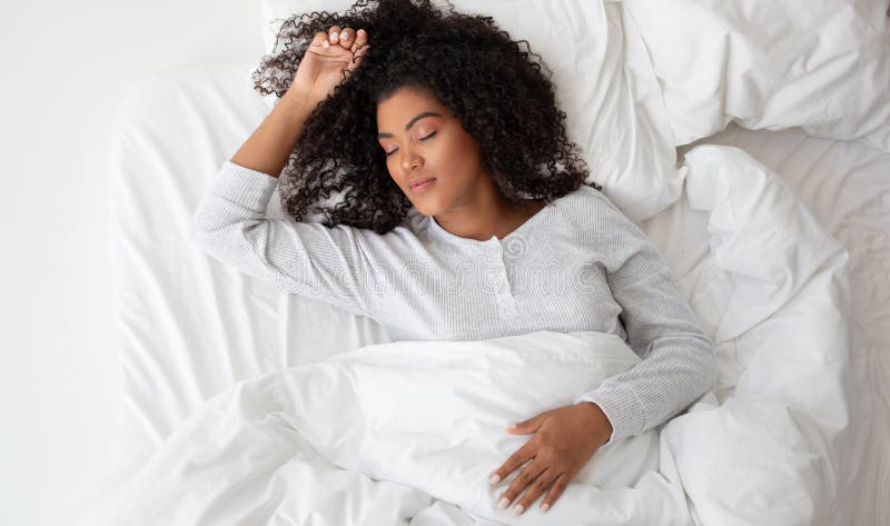 A Hispanic woman is laying comfortably in a bed covered with crisp white sheets. She appears relaxed and is surrounded by a serene atmosphere. A Hispanic woman is laying comfortably in a bed covered with crisp white sheets. She appears relaxed and is surrounded by a serene atmosphere.