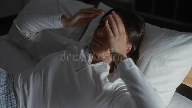 Femme allongée dans la chambre à coucher tenant tête dans l'inconfort avec les mains sur son visage jeune hispanique brune femme e banque de vidéos