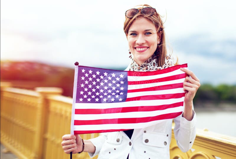 Femme américaine de jeune patriote avec le sourire toothy étirant le drapeau des Etats-Unis photographie stock Femme américaine de jeune patriote avec le sourire toothy étirant le drapeau des Etats-Unis photographie stock