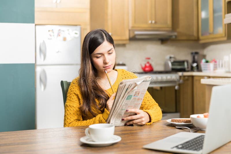 Young woman thinking while solving crossword puzzle at table during breakfast time. Young woman thinking while solving crossword puzzle at table during breakfast time