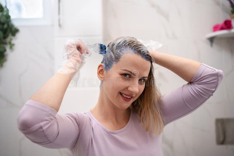 Femme appliquant un teint pourpre à la maison dans la salle de bain photos stock