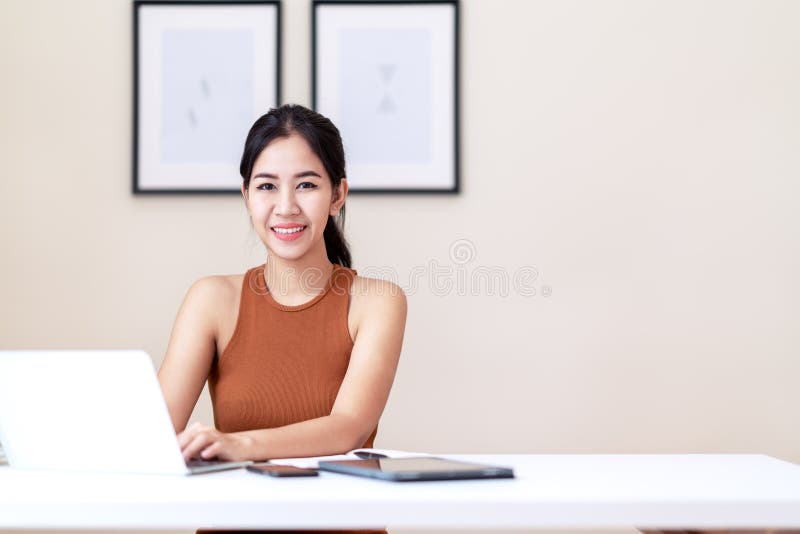 Femme asiatique attirante d'entrepreneur, étudiant heureux ou jeune exécutif s'asseyant sur la table blanche de bureau portant la