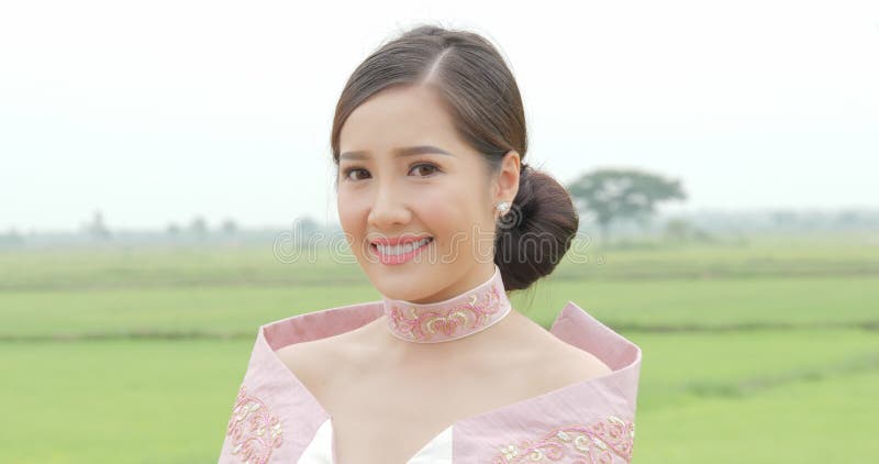 Femme asiatique attirante dans la tête de rotation de costume asiatique du sud-est traditionnel à la caméra et sourire sur un fon clips vidéos