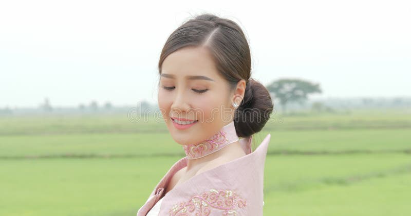 Femme asiatique attirante dans la tête de rotation de costume asiatique du sud-est traditionnel à la caméra et sourire sur un fon clips vidéos