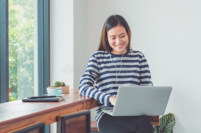 Femme asiatique heureuse employant sur l'ordinateur portable et la musique de écoute W images libres de droits Femme asiatique heureuse employant sur l'ordinateur portable et la musique de écoute W images libres de droits