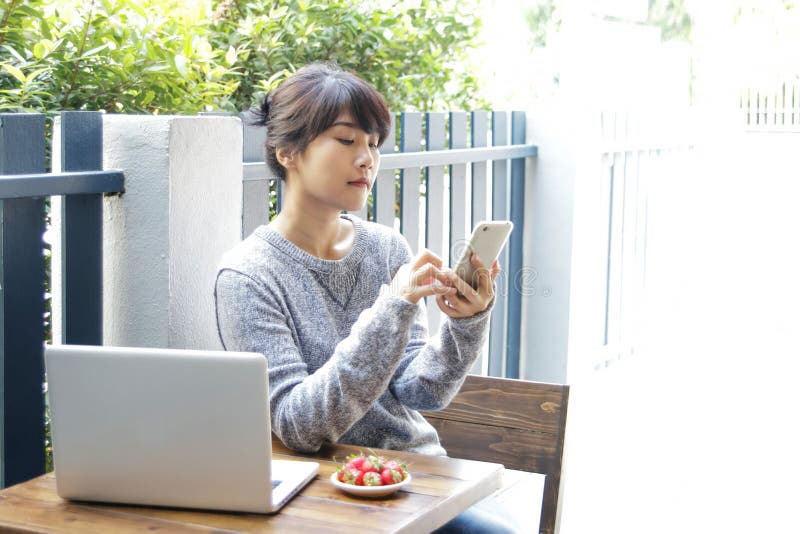 Femme asiatique s'asseyant à une table et à l'aide du smartphone à la maison Type photographie stock libre de droits Femme asiatique s'asseyant à une table et à l'aide du smartphone à la maison Type photographie stock libre de droits