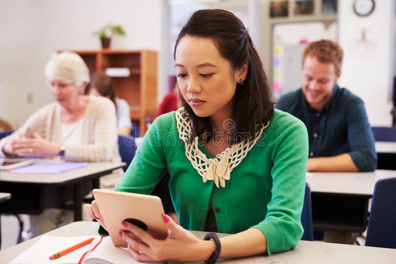Femme asiatique à l'aide de la tablette dans la classe d'éducation des adultes image stock Femme asiatique à l'aide de la tablette dans la classe d'éducation des adultes image stock