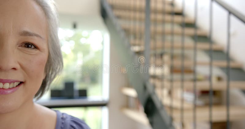 Femme asiatique âgée souriante debout dans une maison moderne avec escalier en arrière-plan banque de vidéos